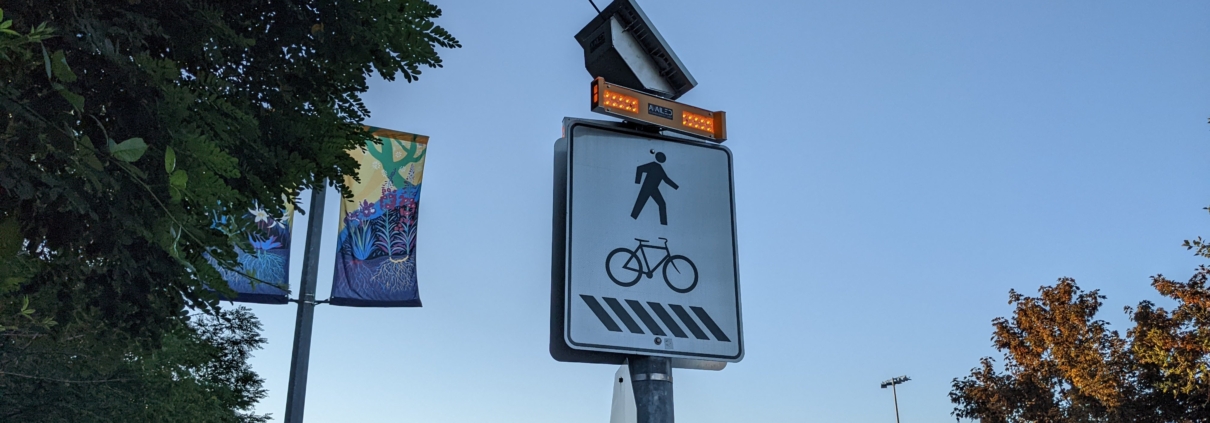 Pedestrian and bicycle crossing sign with solar-powered flashing lights on top at a street intersection